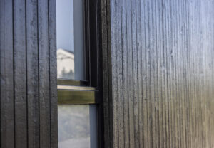 Nærbilde av stående ULTIMALT dobbelfals rett 10 mm kledning malt med Jotun 9918 Dempet Sort, med vindusprofil som gir en kontrast og fremhever det moderne og minimalistiske uttrykket.